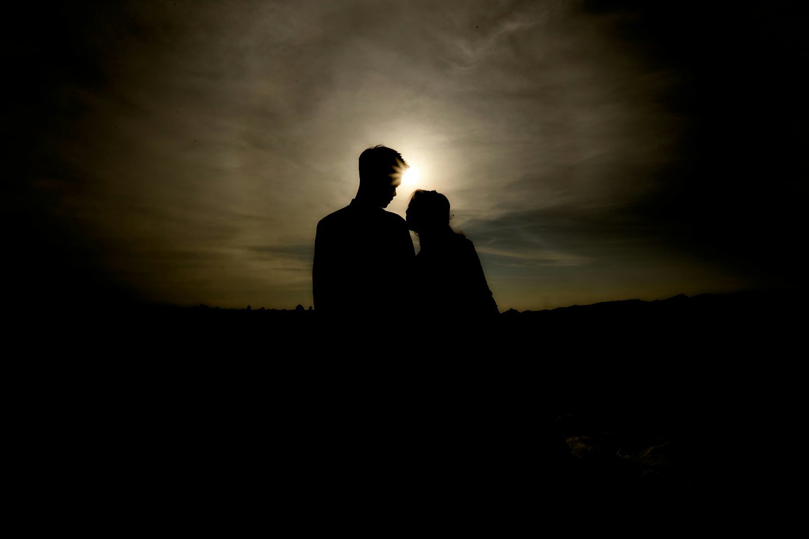 silhouette of man and woman standing on field during sunset